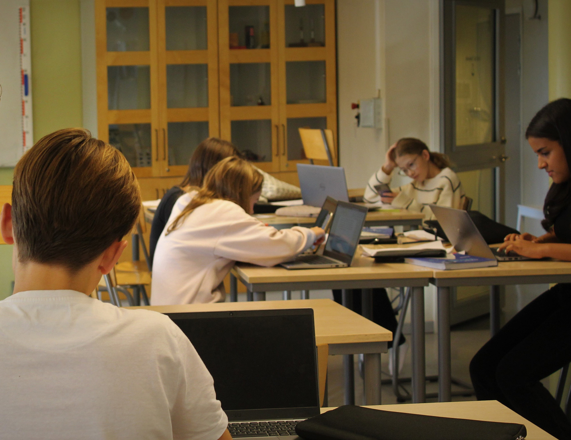 Fem skolelever som använder datorn som arbetsredskap under lektionstid